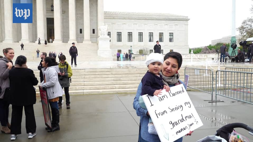 Woman holding baby who holds a sign saying "I am banned from seeing my grandma!"